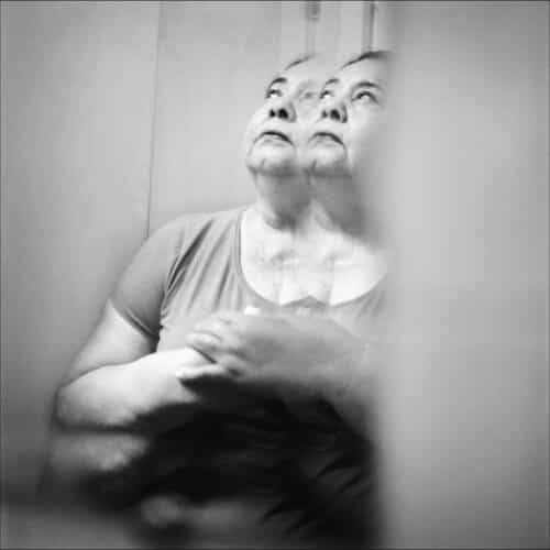 Retrato en blanco y negro de una mujer mayor con el rostro duplicado por un efecto de reflejo.