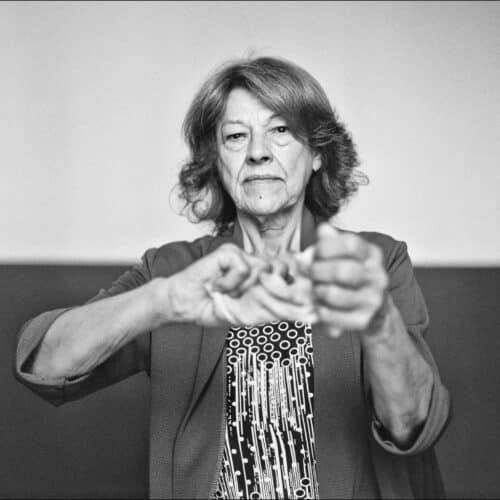 Mujer mayor mirando al frente mientras sostiene un objeto entre las manos extendidas.