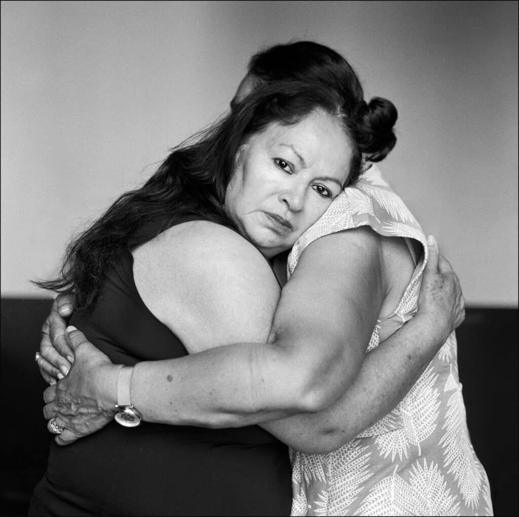 Dos mujeres se abrazan con fuerza; una de ellas mira directamente a la cámara.
